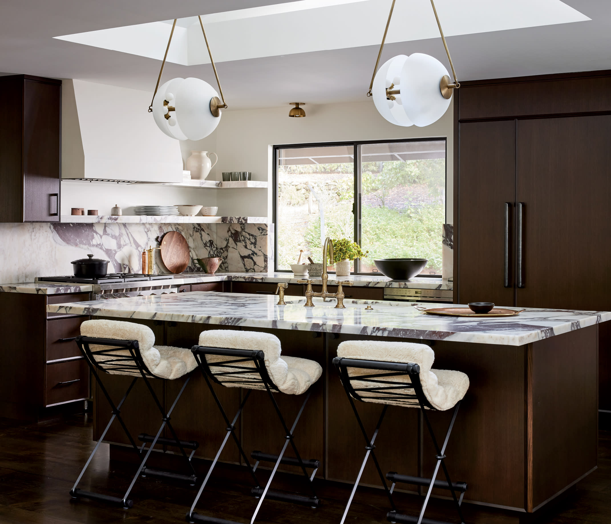 dark wood kitchen with sheepskin-upholstered counter stools and circular pendant lights